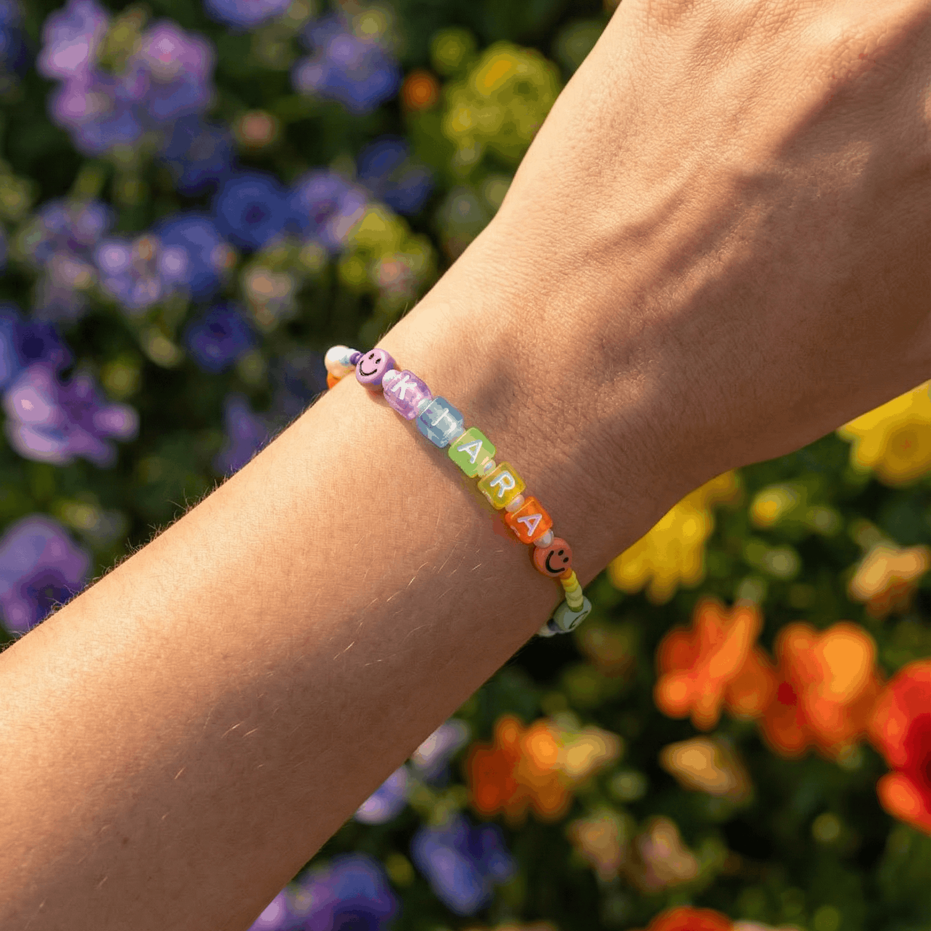 Personalisiertes Armband mit bunten Perlen am Handgelenk vor Blumen im Hintergrund